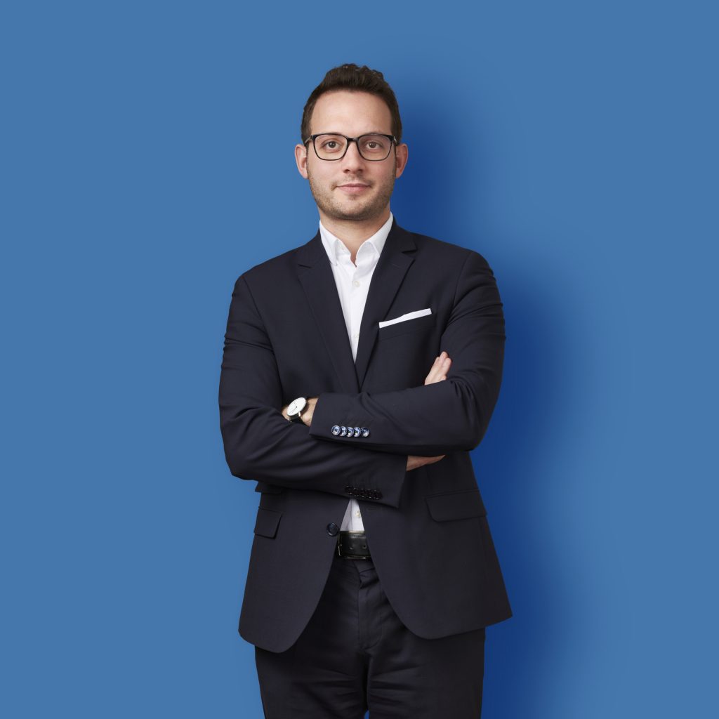 photographe Photographe homme en costume sombre, lunettes, pose mode beauté, fond bleu uni, portrait professionnel à Paris. Paris