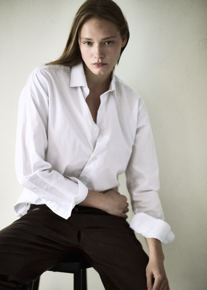photographe Portrait mode par un photographe à Paris : personne aux longs cheveux, chemise blanche ample, pantalon sombre, pose assise studio. Paris