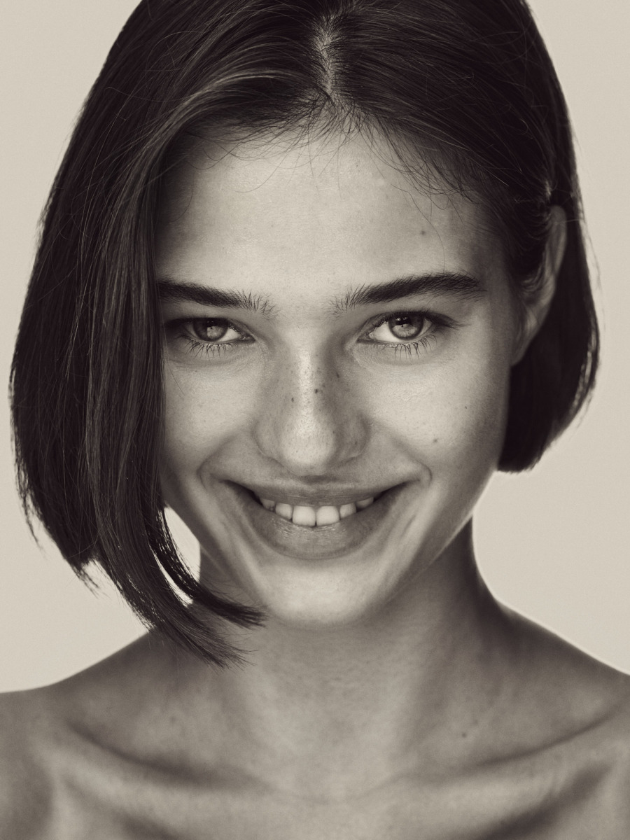 photographe Portrait de beauté en noir et blanc d’une jeune femme photographe à Paris, aux cheveux courts et foncés, à la peau claire parsemée de légères taches de rousseur, dont le regard direct s’accompagne d’un doux sourire. Idéal pour un book de mannequin ou un portfolio lifestyle. Paris